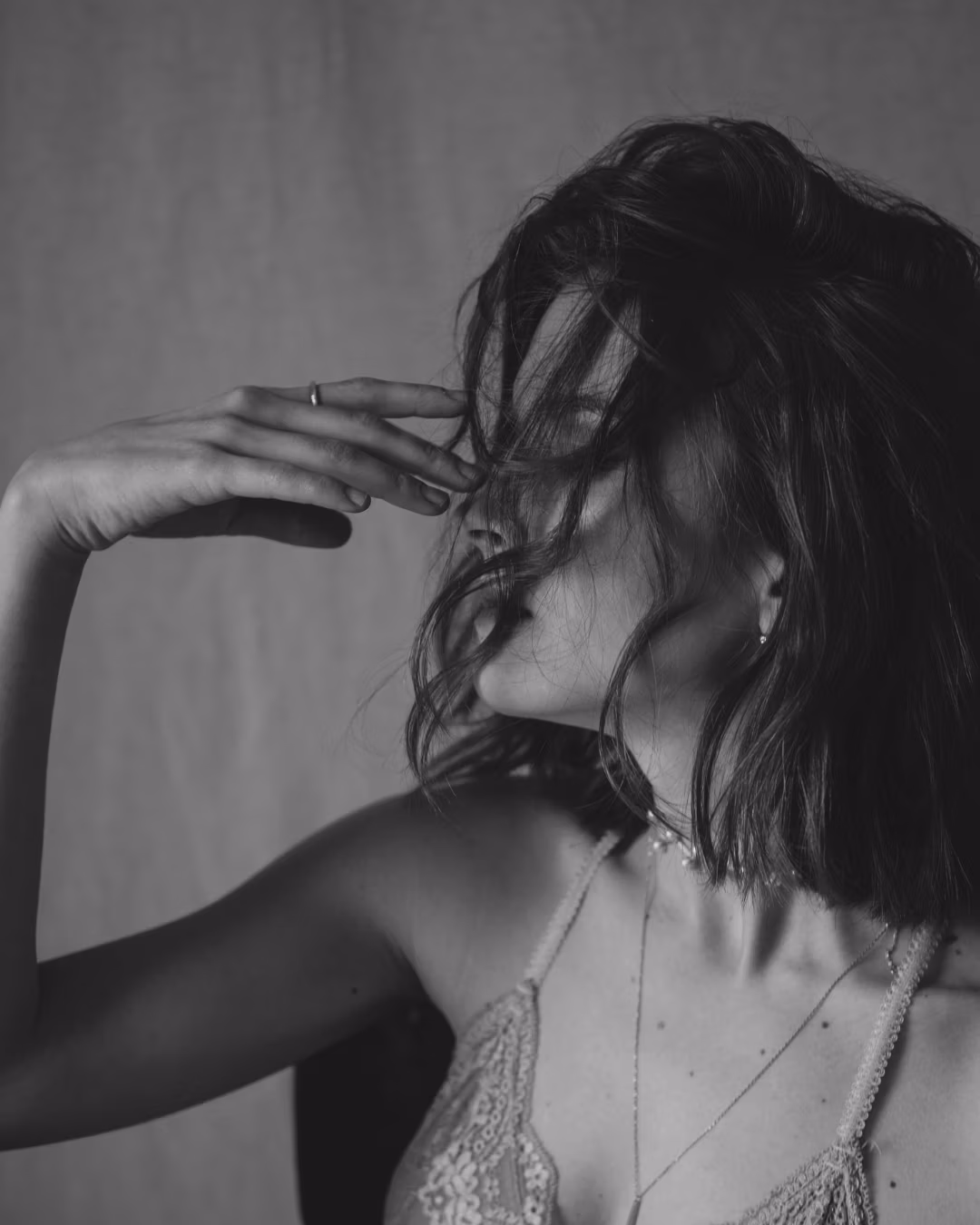 Black and white photo of a woman adjusting her hair against a plain background